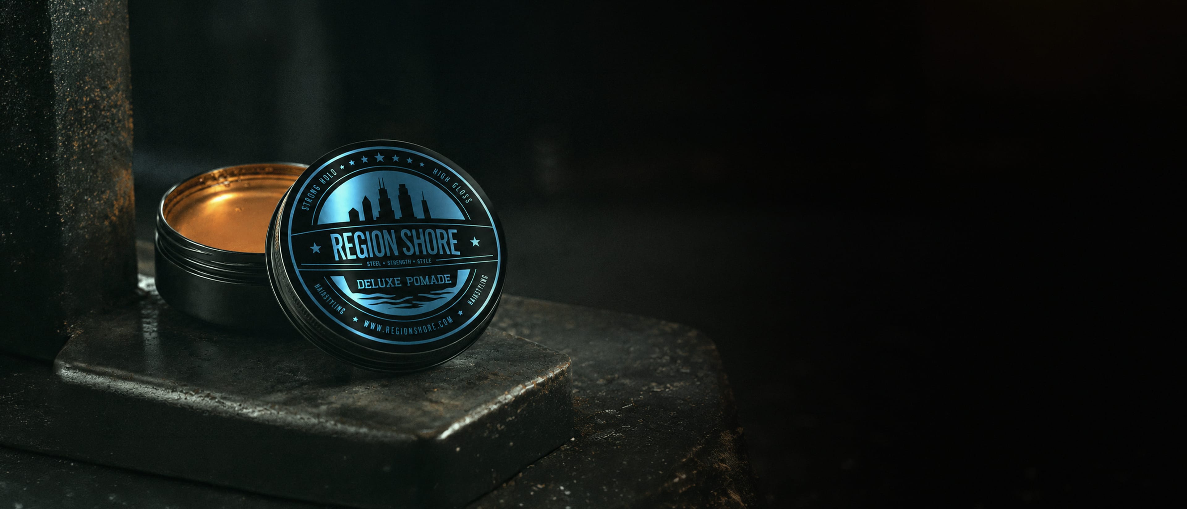 Open Region Shore deluxe pomade tin on a dark industrial surface