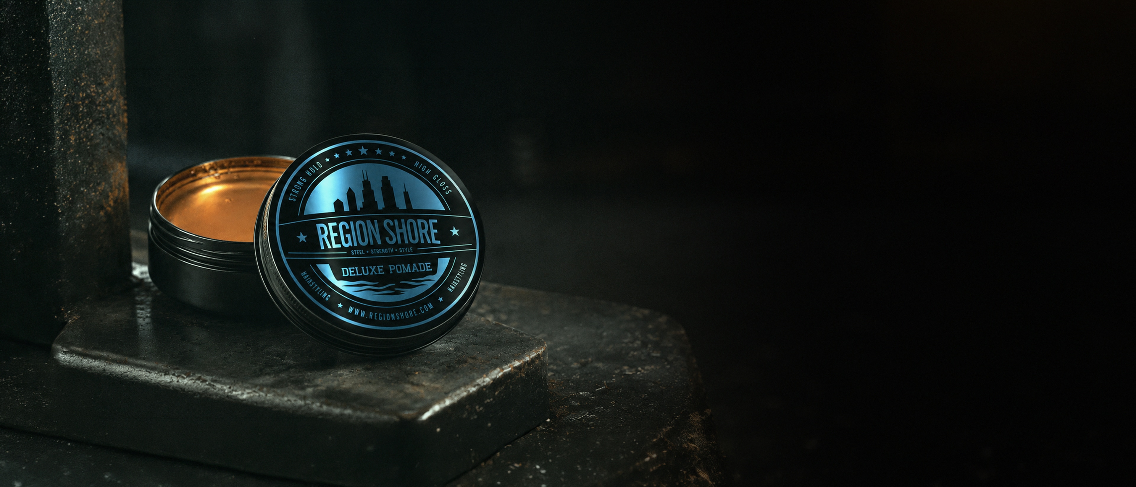 Open Region Shore deluxe pomade tin on a dark industrial surface